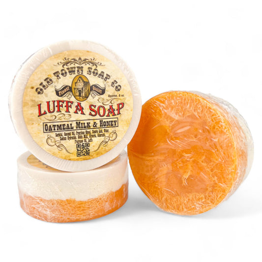 Luffa Soap, a round white goat’s milk soap with an orange natural loofah core and a vintage-style printed label.
