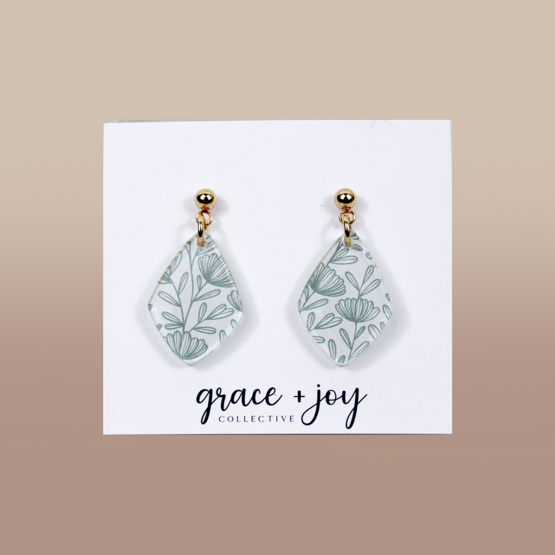 Green and White wildflower dangle earrings in white acrylic with delicate sage-green botanical line patterns and gold-tone studs.