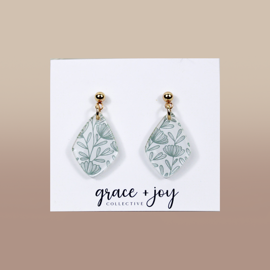 Green and White wildflower dangle earrings in white acrylic with delicate sage-green botanical line patterns and gold-tone studs.