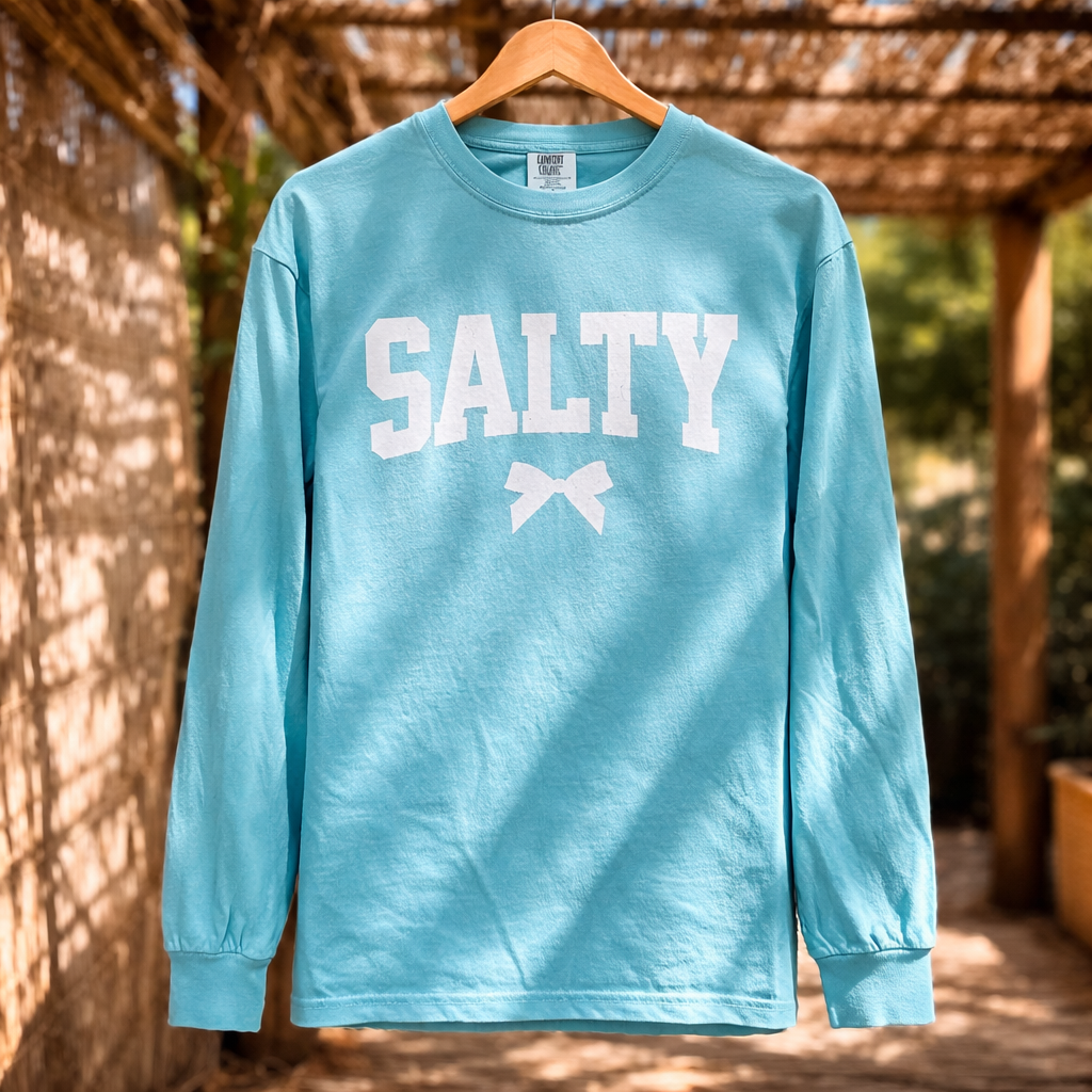Long-sleeve turquoise Salty L/S Comfort Colors tee with bold white “SALTY” lettering and a bow graphic on the chest.