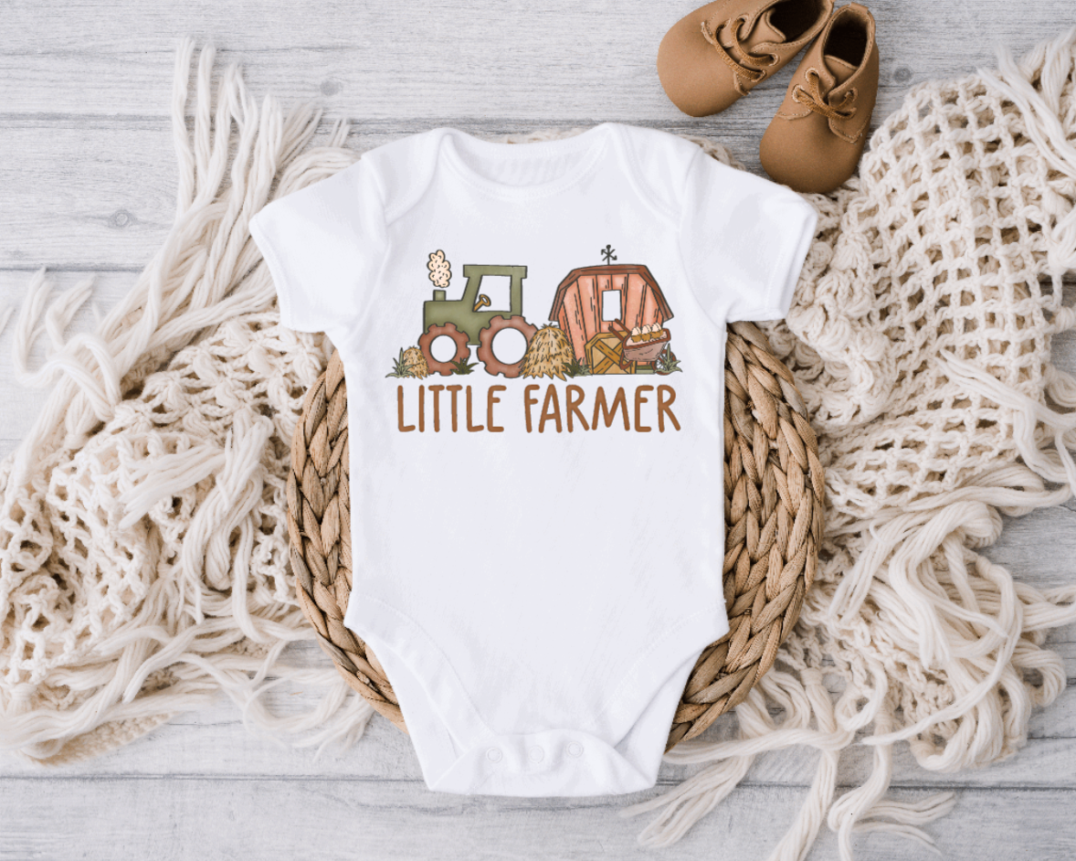 Baby bodysuit in white cotton with a colorful tractor and barn print above “LITTLE FARMER”; Little Farmer Cute Farm