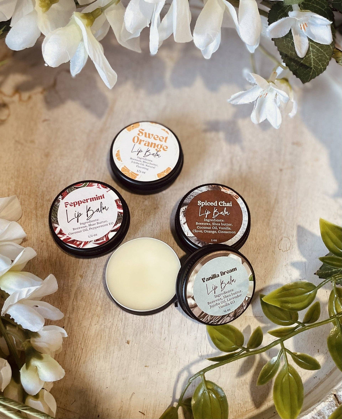 Natural Lip Balm in round black tins, with white, orange, brown and pale green labels and an open tin of cream balm.